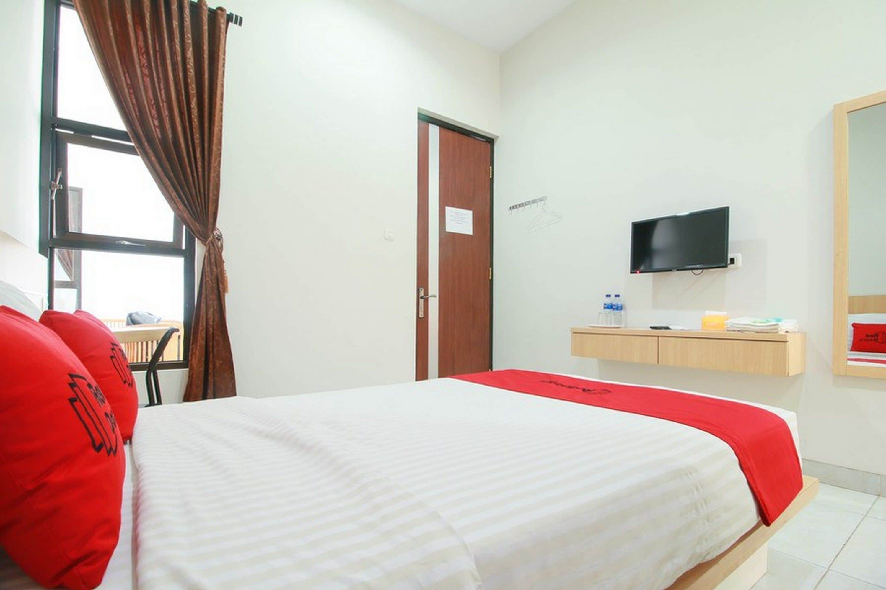 A hotel room with a bed, a TV, a desk, and a window with curtains.