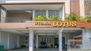 A building with a sign reading "WISMA LOTUS" and a covered parking area with a car and motorcycles. - RedDoorz Syariah near Universitas Jenderal Soedirman (Purwokerto)
