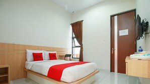 A hotel room with a bed, a desk, a chair, a window with curtains, and a door. - RedDoorz Syariah near Universitas Jenderal Soedirman (Purwokerto)