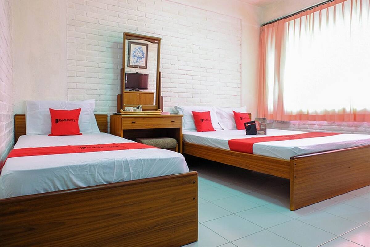A hotel room with two wooden beds, a nightstand, a mirror, and a window with curtains.