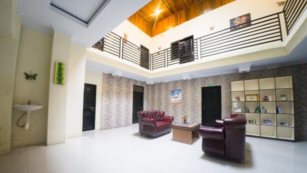 A spacious lobby with a high ceiling, a central seating area with two leather sofas, a small table, and a decorative shelf with books and items. - RedDoorz Syariah near RSUD Ainun Habibie Gorontalo (Limboto)