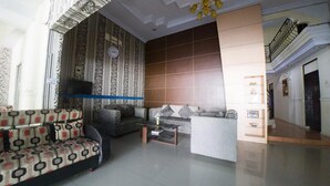 A spacious living room with patterned sofas, a coffee table, and a decorative wall with a clock. - RedDoorz Syariah near RSUD Ainun Habibie Gorontalo (Limboto)