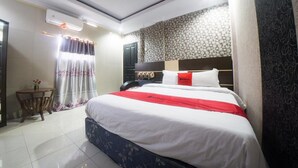 A hotel room with a large bed, a bedside table, a chair, and a small table with a vase. - RedDoorz Syariah near RSUD Ainun Habibie Gorontalo (Limboto)