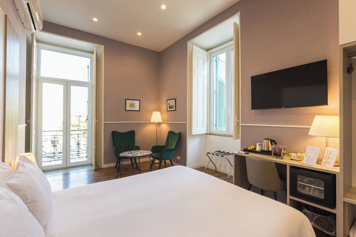 Camera d'albergo con un letto, una scrivania, una sedia, una televisione e un balcone con vista.