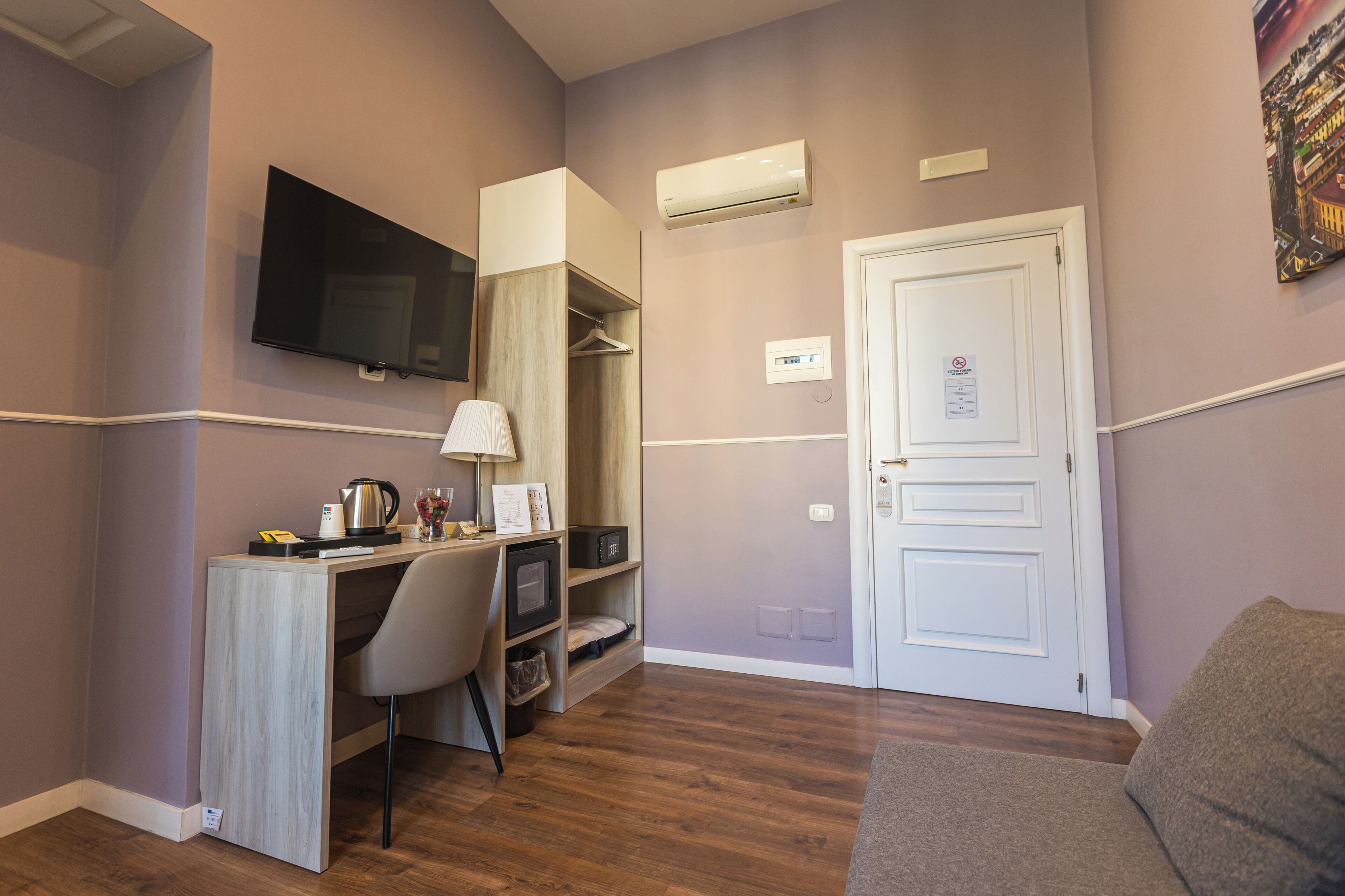 A compact room with a wooden desk, a chair, a television, an air conditioner, and a door with a sign.