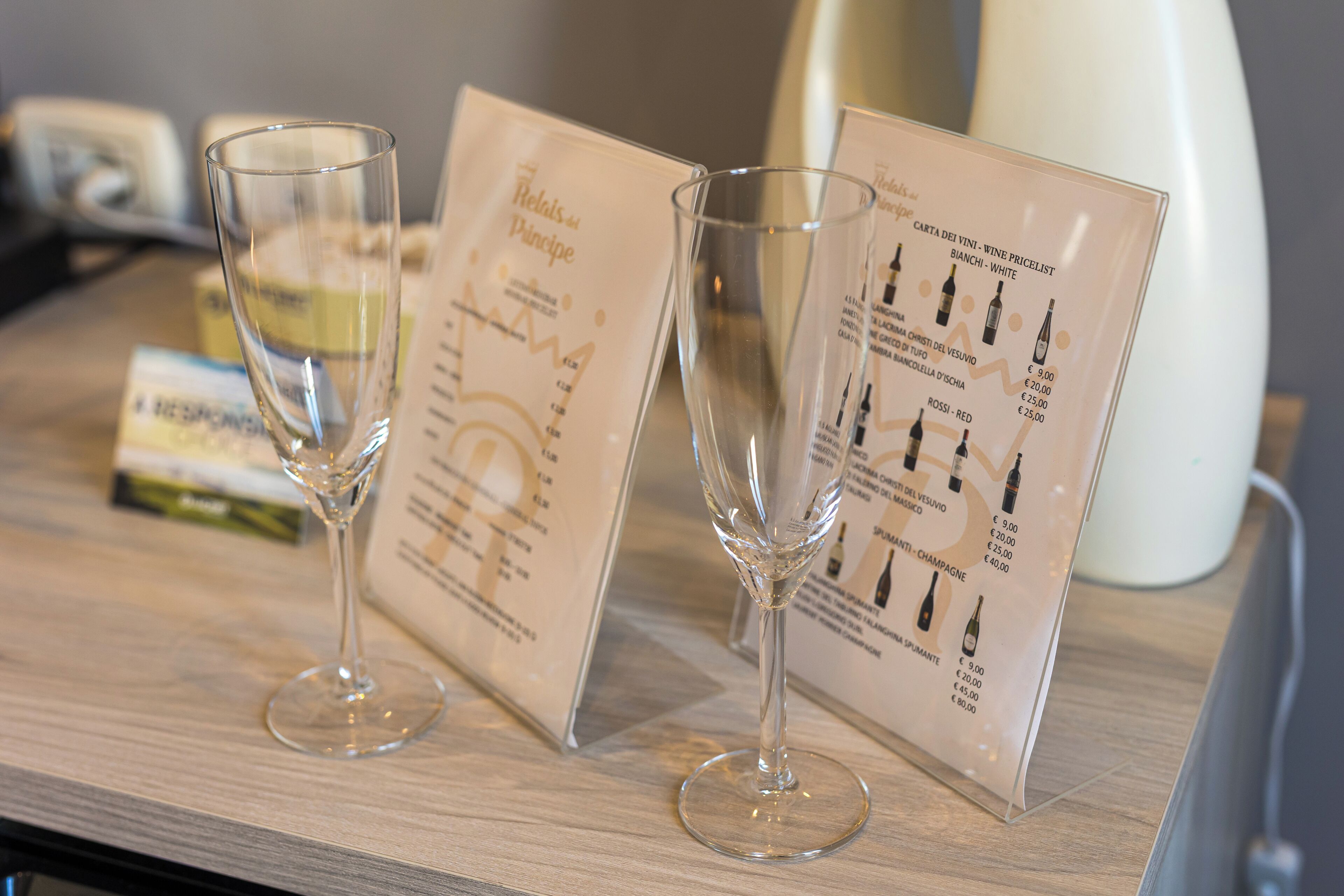 Deux verres à vin vides sont posés sur une table en bois, à côté de menus indiquant les prix des vins.
