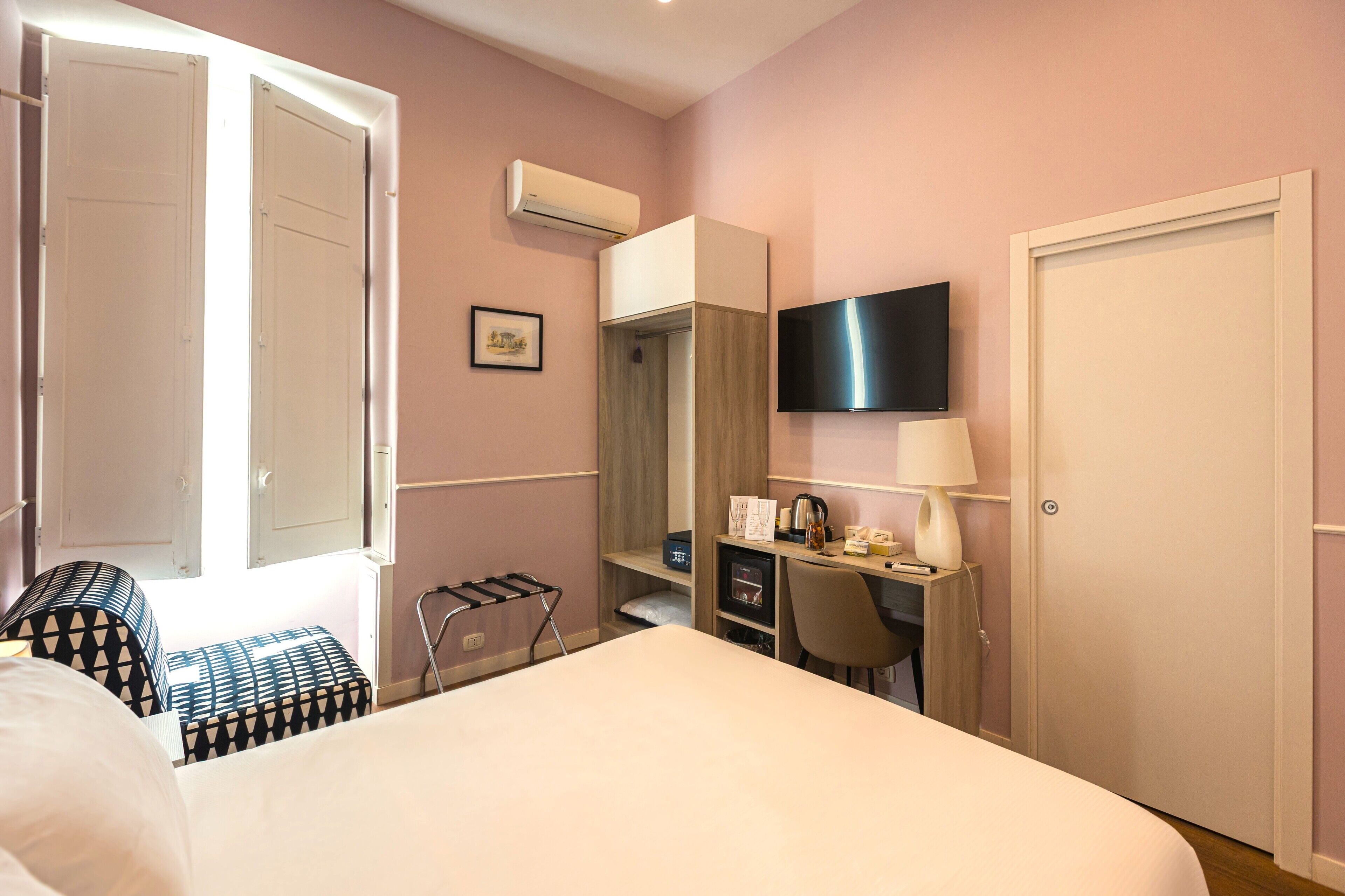 Een hotelkamer met een bed, bureau, stoel, televisie en garderobe.