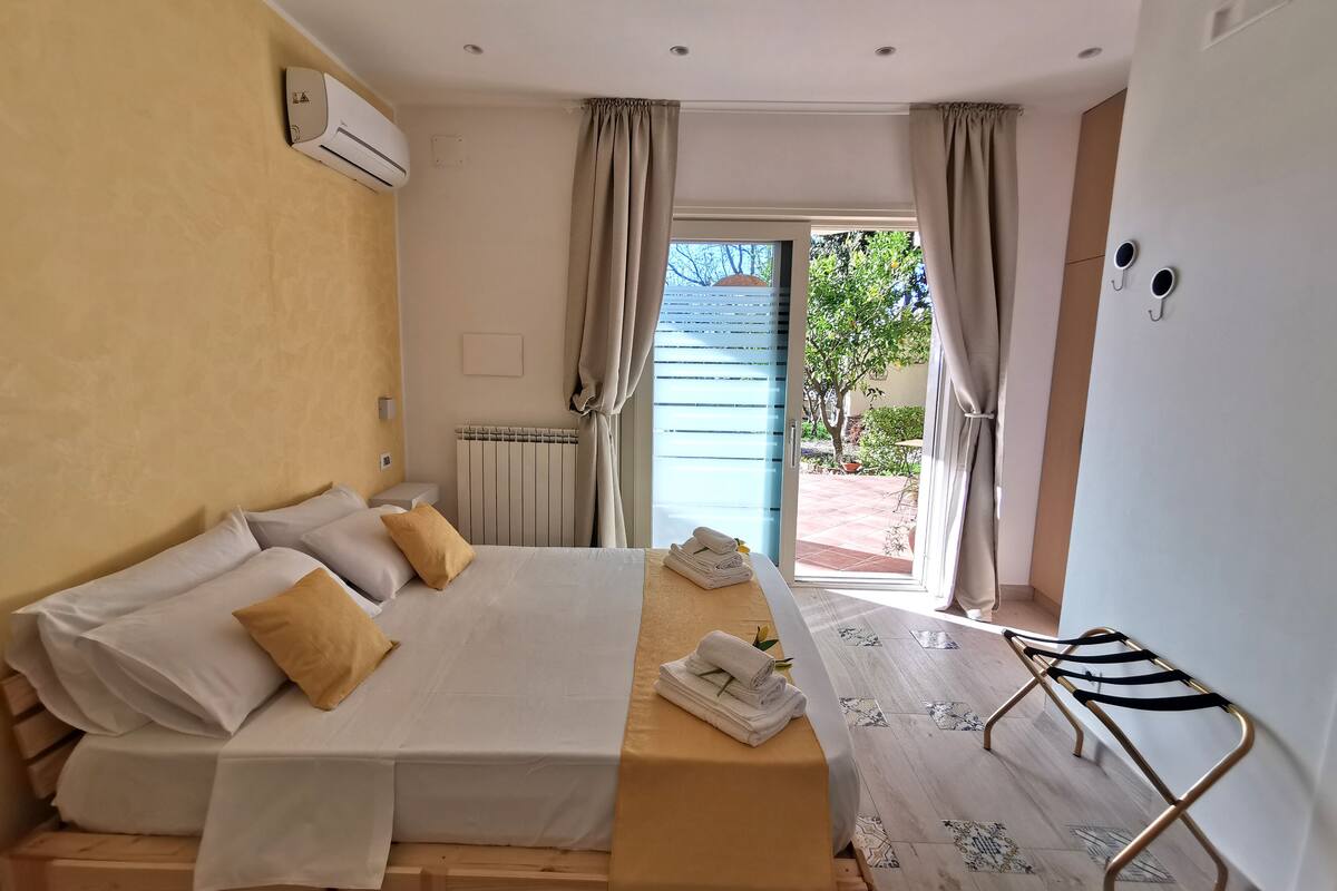 A bedroom with a bed, a radiator, a window with curtains, and a view of the outside.