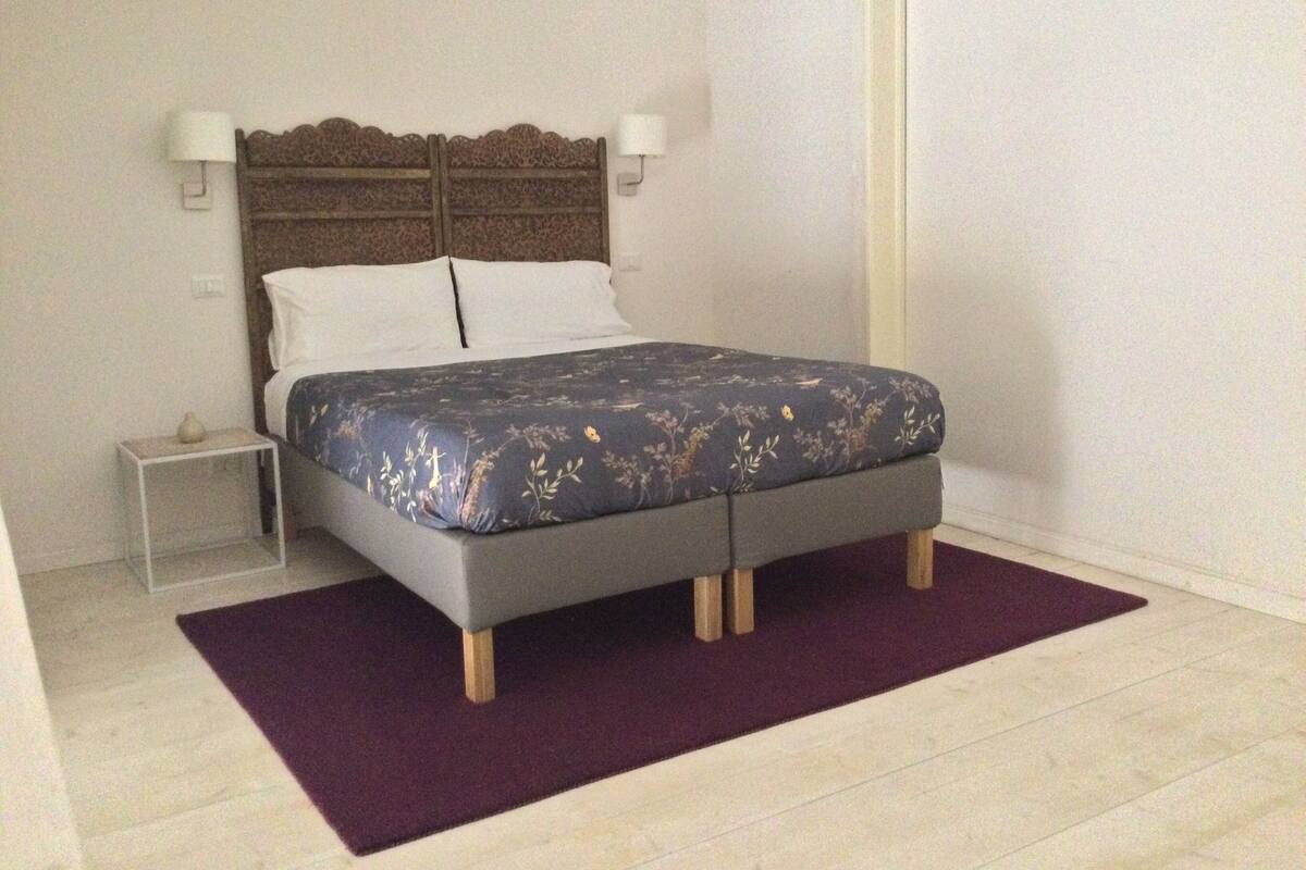 A bedroom with a bed, nightstand, and wall-mounted lamps.