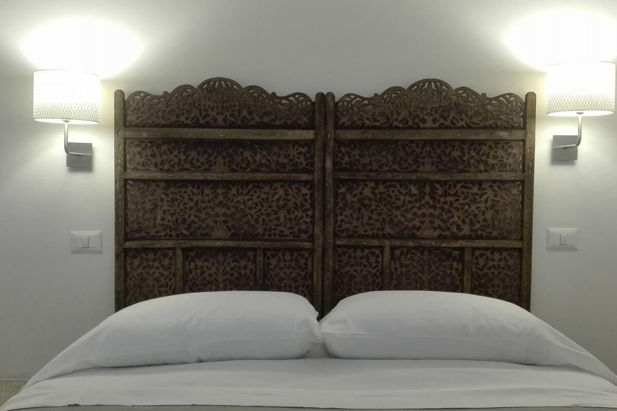 A bed with a decorative headboard, two wall-mounted lamps, and a switch on the wall.