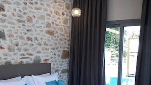 Un dormitorio con pared de piedra, cama con ropa de cama blanca y azul, y vistas a través de un ventanal grande.