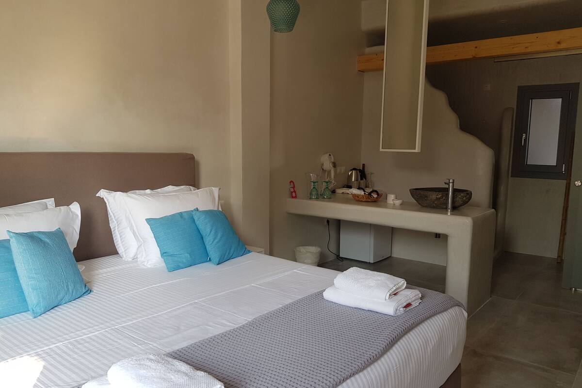 Ein ordentlich bezogenes Bett mit weißen und blauen Kissen, einer grauen Decke und einem gefalteten Handtuch.