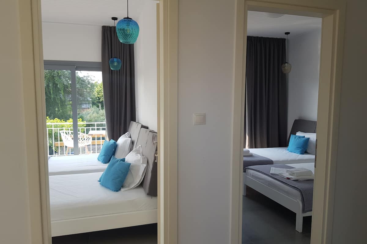 Ein Hotelzimmer mit zwei Betten, jeweils mit blau-weißer Bettwäsche, und einem Balkon mit Blick auf Grünflächen.