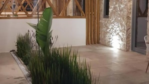 Un interior moderno con techo de madera, pared de piedra y una planta verde grande en el centro.