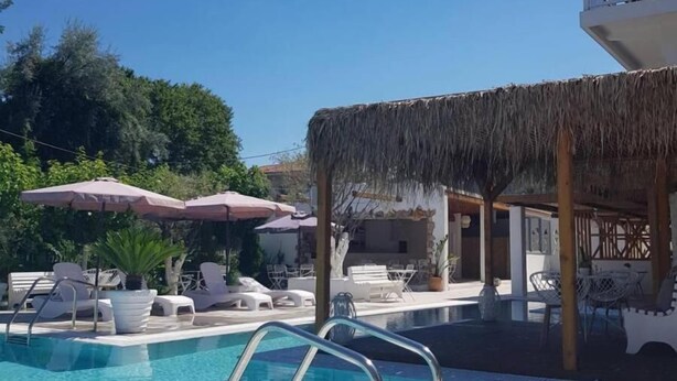Un área de piscina con sillones de descanso, sombrillas y una estructura de techo de paja.