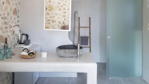 Un baño con pared de piedra, lavamanos blanco, espejo y techo de madera.