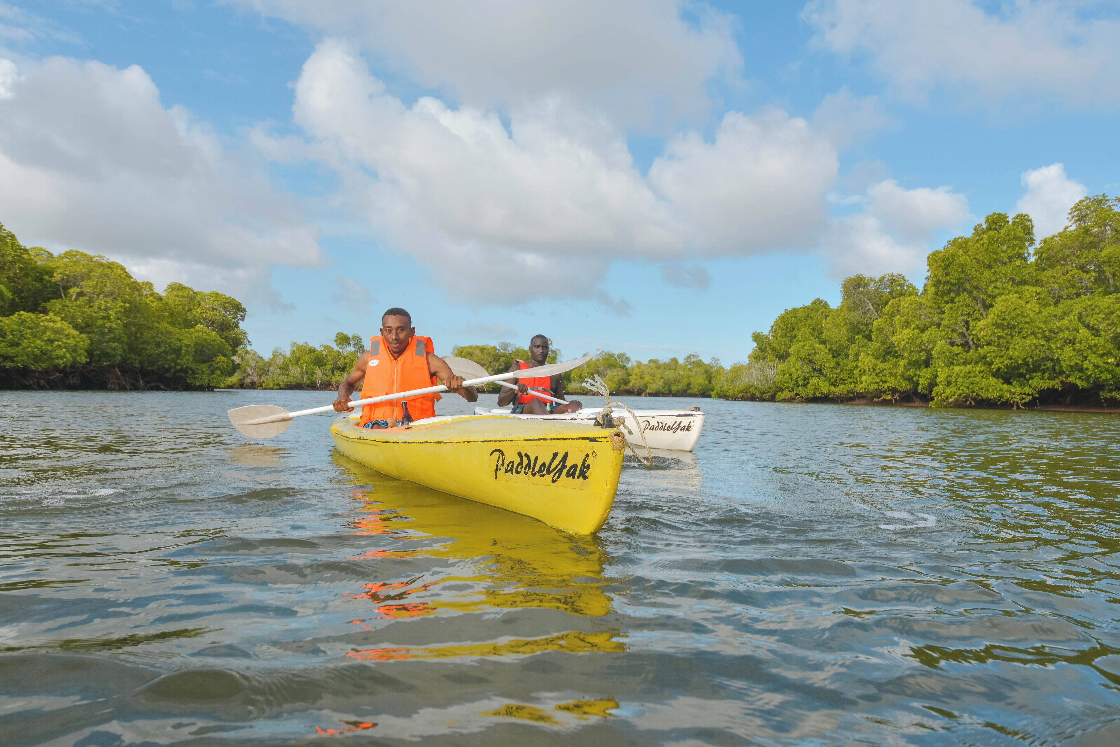 A yellow kayak with 'Paddlejak' written on it, two people paddling, surrounded by calm water and greenery.