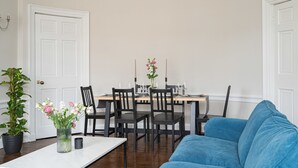 A dining area with a table set for four, surrounded by chairs, and a blue sofa in the foreground. - Warriston Crescent Apartment (Edinburgh)