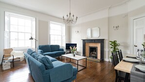 A living room with a blue sofa, a coffee table, a fireplace, and a dining area with chairs and a table. - Warriston Crescent Apartment (Edinburgh)