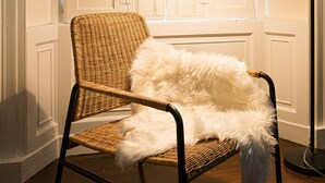 A wicker chair with a fluffy white pillow, a floor lamp, and a stack of books and a mug on the floor. - Warriston Crescent Apartment (Edinburgh)