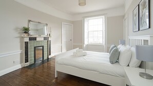 A bedroom with a white bed, a fireplace, a large window, and a wall-mounted mirror. - Warriston Crescent Apartment (Edinburgh)
