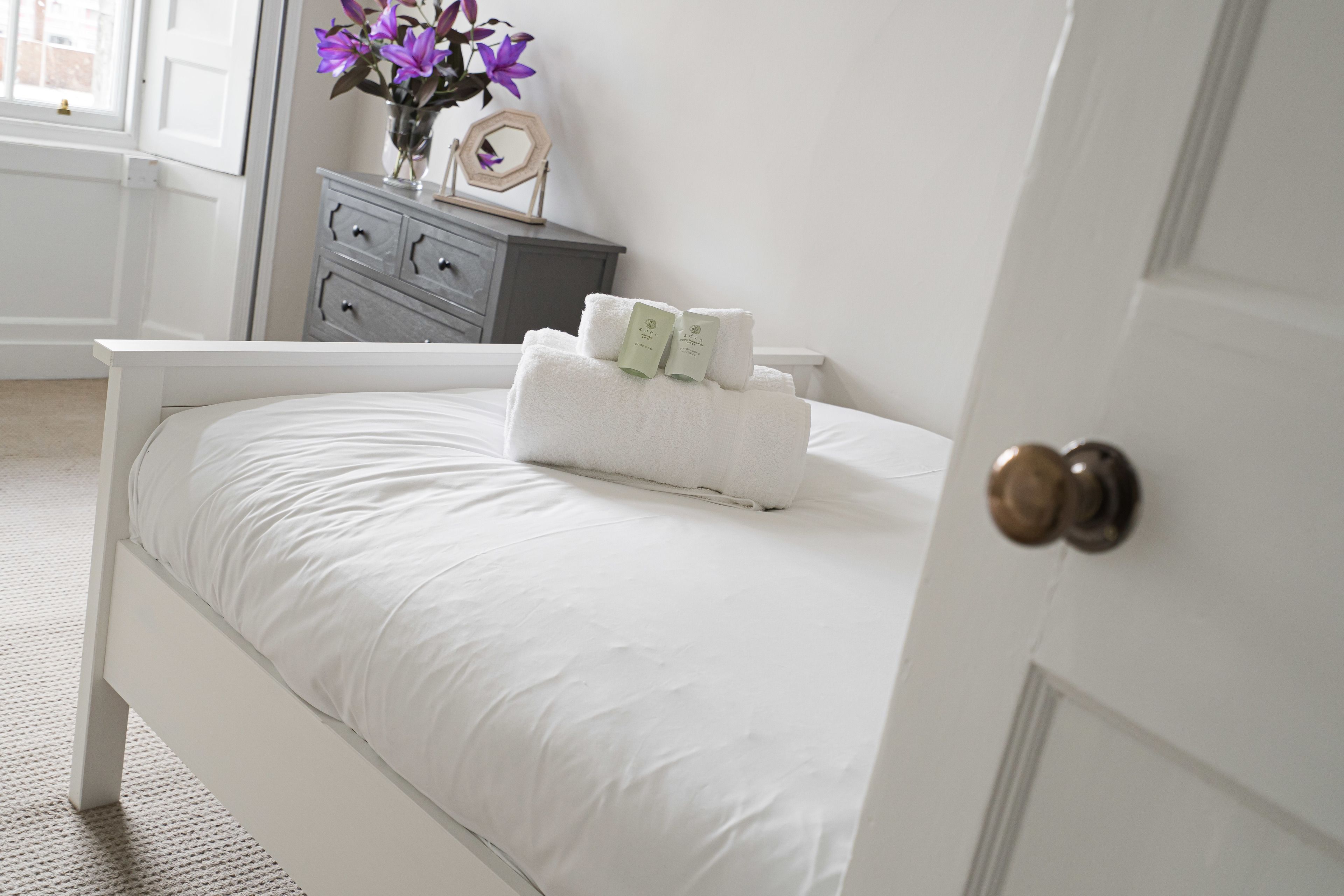 A neatly made bed with white linens and two towels placed on top.