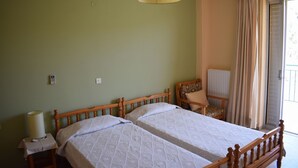 A room with two beds, a chair, a lamp, and a window with curtains. - Apartments Rania (Nafplio)