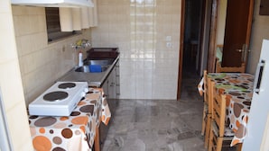 A compact kitchen with a stove, sink, and tiled backsplash. There is a dining area with a table and chairs. - Apartments Rania (Nafplio)
