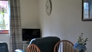 Un coin repas avec une table et des chaises en bois, un canapé, un téléviseur et une horloge au mur.