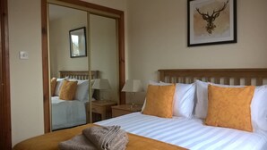 Une chambre d’hôtel avec un grand lit, deux lampes de chevet, un miroir et une œuvre d’art représentant une tête de cerf encadrée, accrochée au mur.