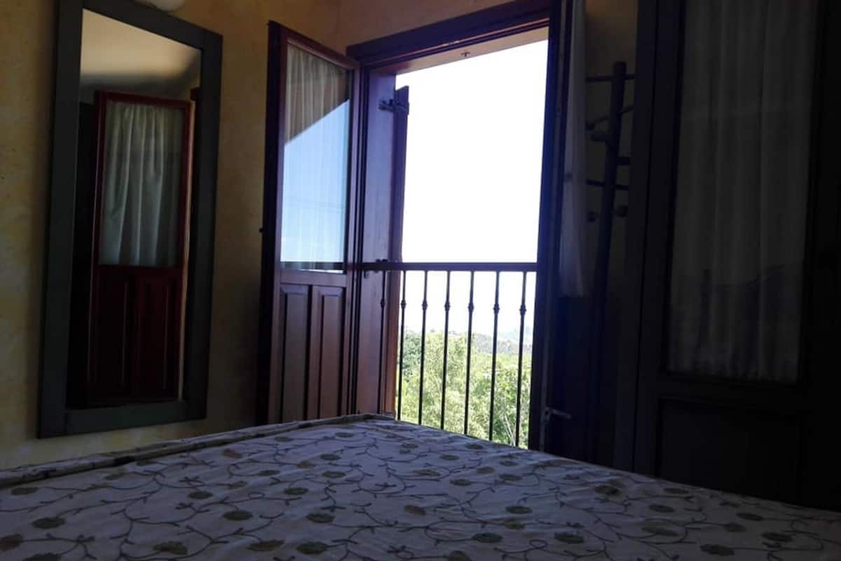 Una habitación con cama, puerta y balcón con barandilla.