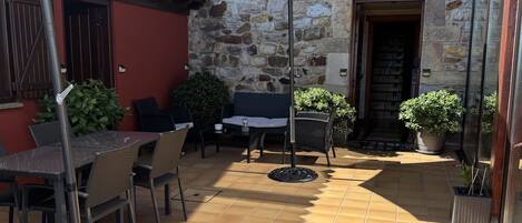 An outdoor patio with tiled flooring, a table with chairs, a large umbrella, and potted plants.