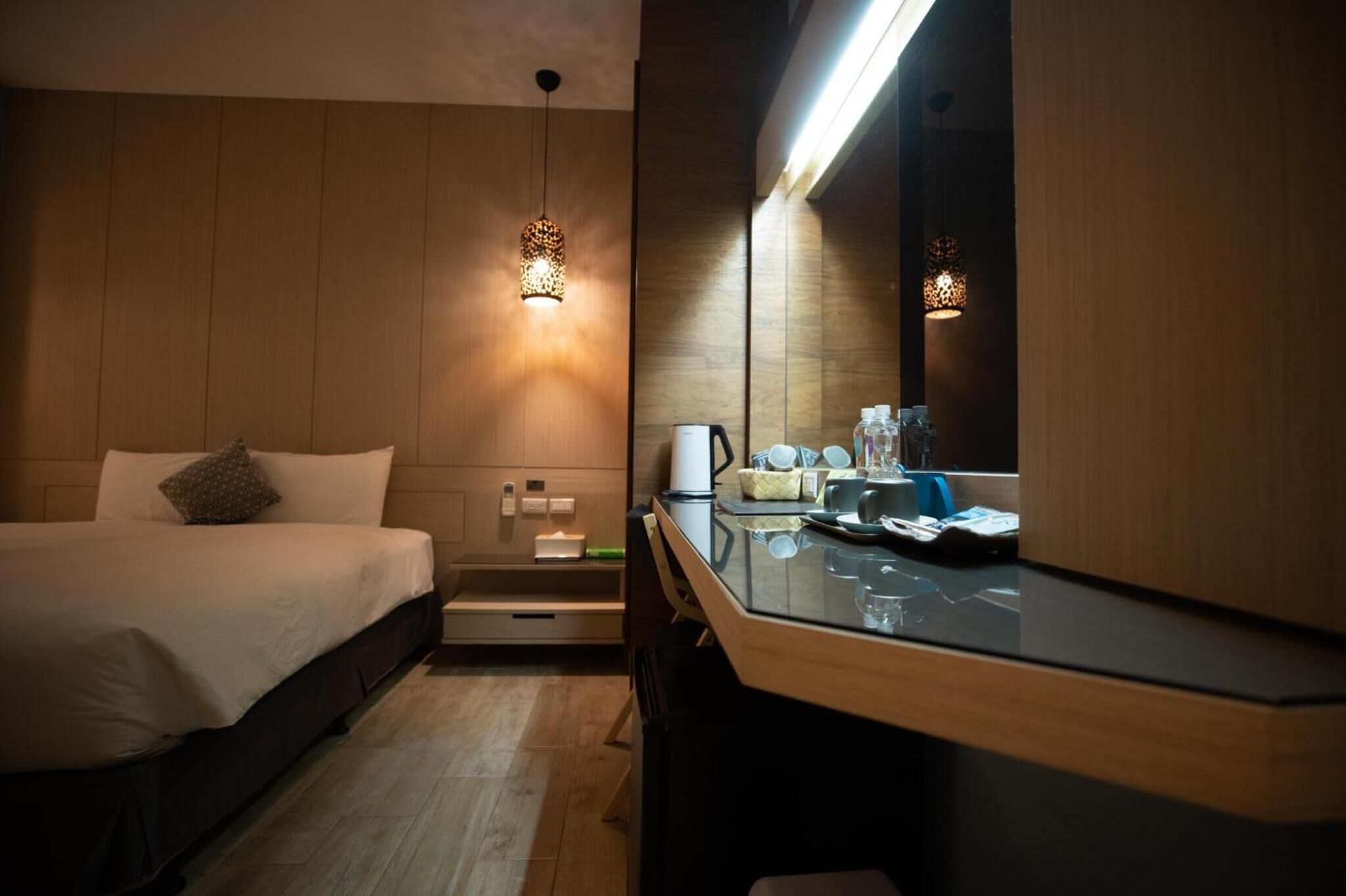 A hotel room with a bed, a desk, a mirror, and a hanging light fixture.
