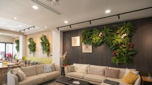 A modern living room with a beige sofa set, a coffee table, and a wall adorned with green foliage and flowers. - Hua B&B (Hengchun)