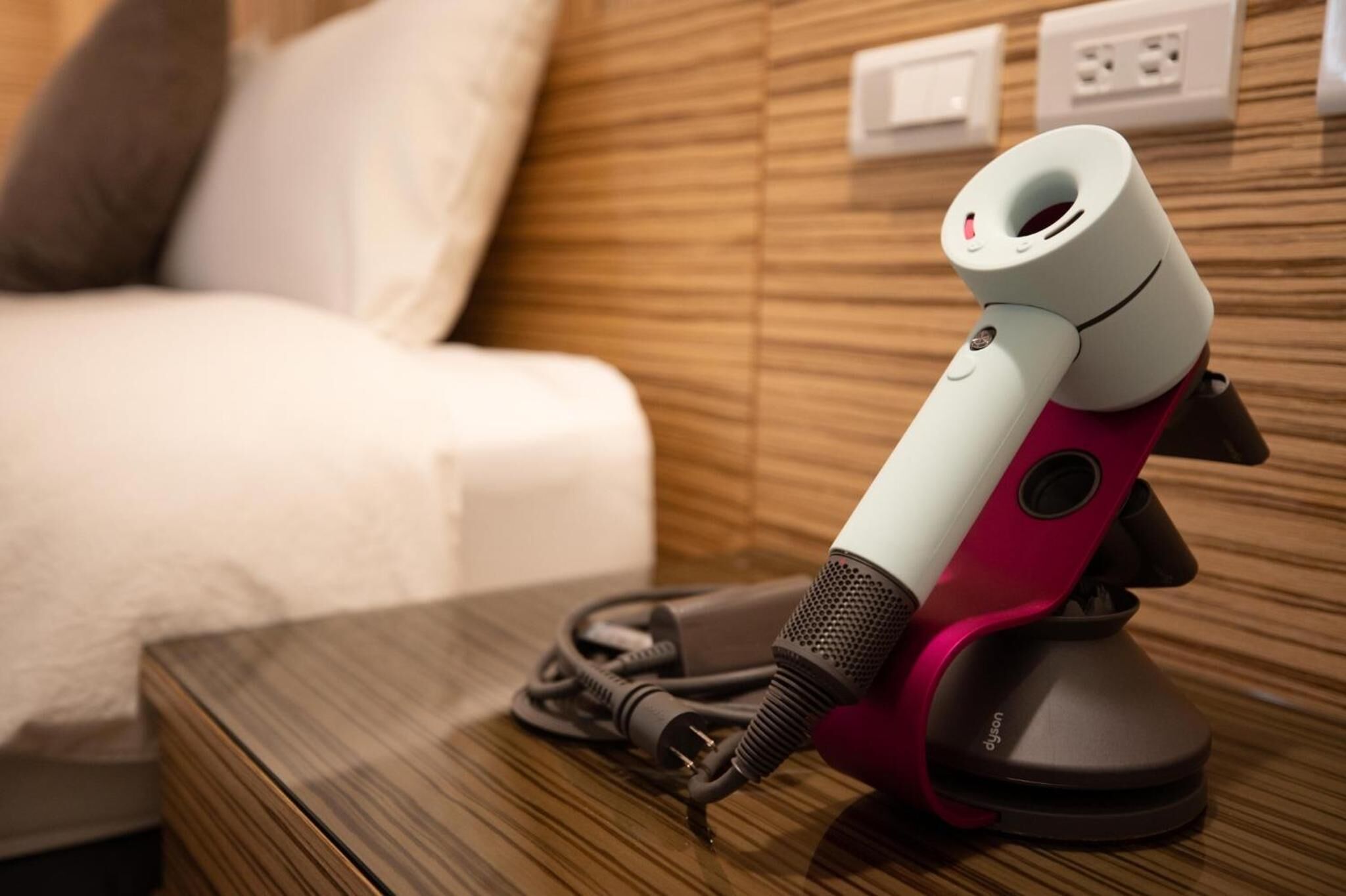 A portable speaker on a wooden nightstand in a hotel room.