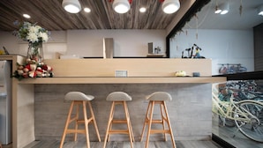 A reception area with a wooden counter, three bar stools, a vase with flowers, and bicycles in the background. - Hua B&B (Hengchun)