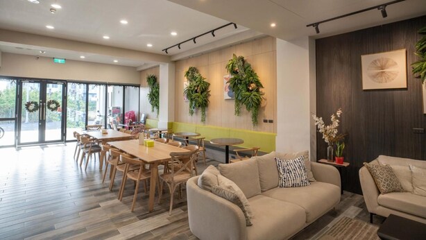 A spacious indoor area with wooden flooring, a sofa, a dining table with chairs, and a wall decorated with greenery. - Hua B&B (Hengchun)