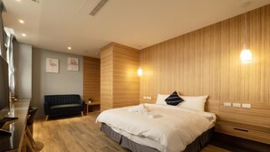 A modern hotel room with a large bed, a sofa, a wooden accent wall, and a dining area. - Hua B&B (Hengchun)