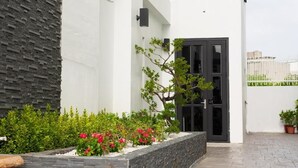 A modern building with a stone facade, a black door, and a garden with red flowers. - Hua B&B (Hengchun)