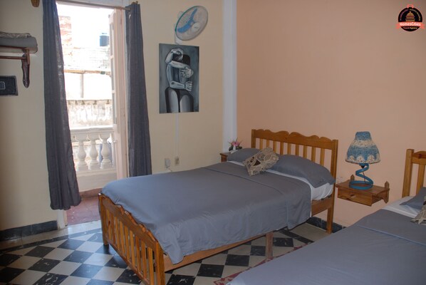 A bedroom with a checkered floor, a bed with a grey bedspread, a bedside table with a lamp, and a painting on the wall. - Alameda dePaula (Havana)