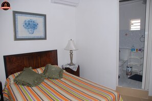 A bed with a striped bedspread, a framed picture on the wall, and a nightstand with a lamp. - Alameda dePaula (Havana)
