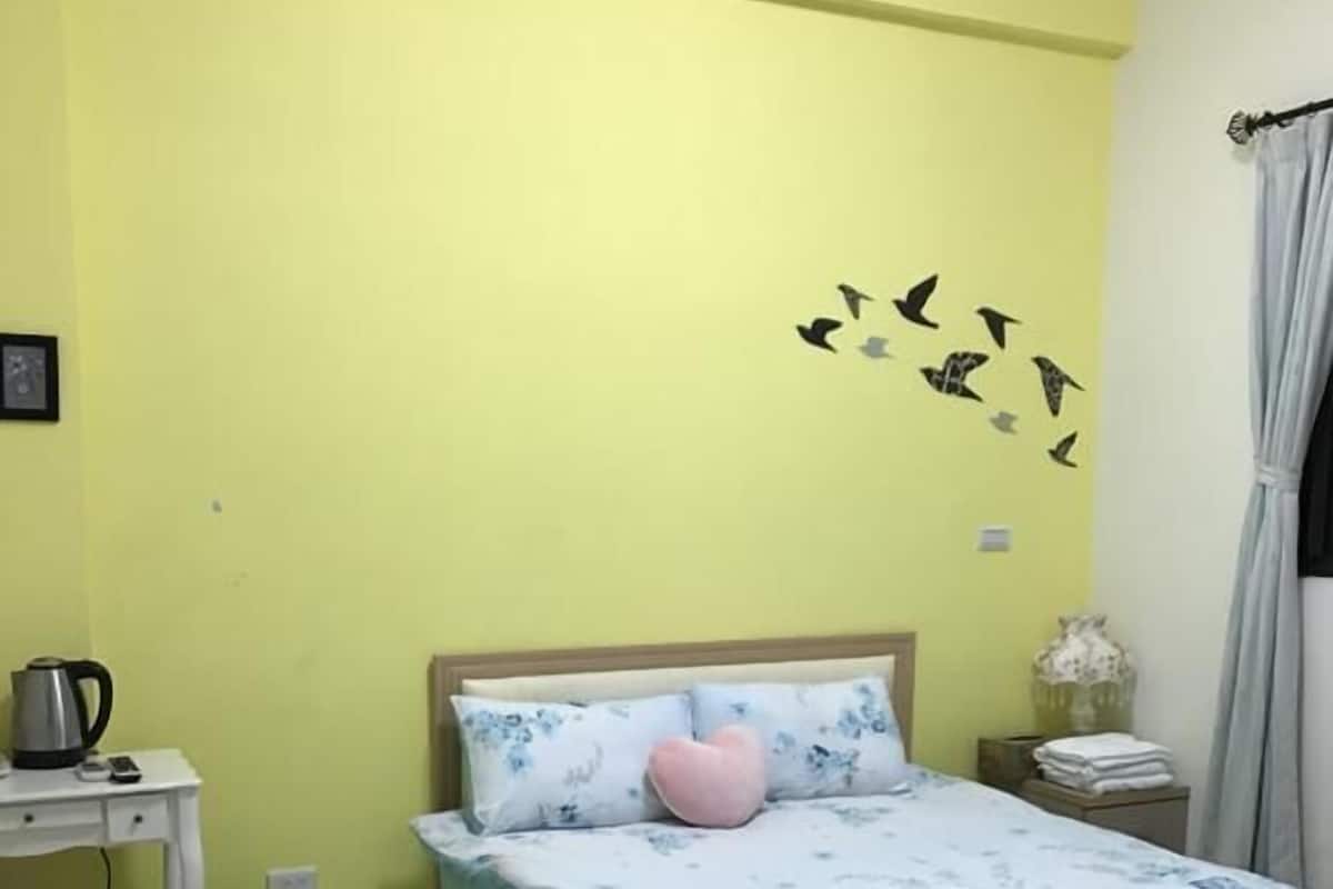 Een slaapkamer met een bed, een bureau, een stoel, een nachtkastje en een muursticker van vogels.