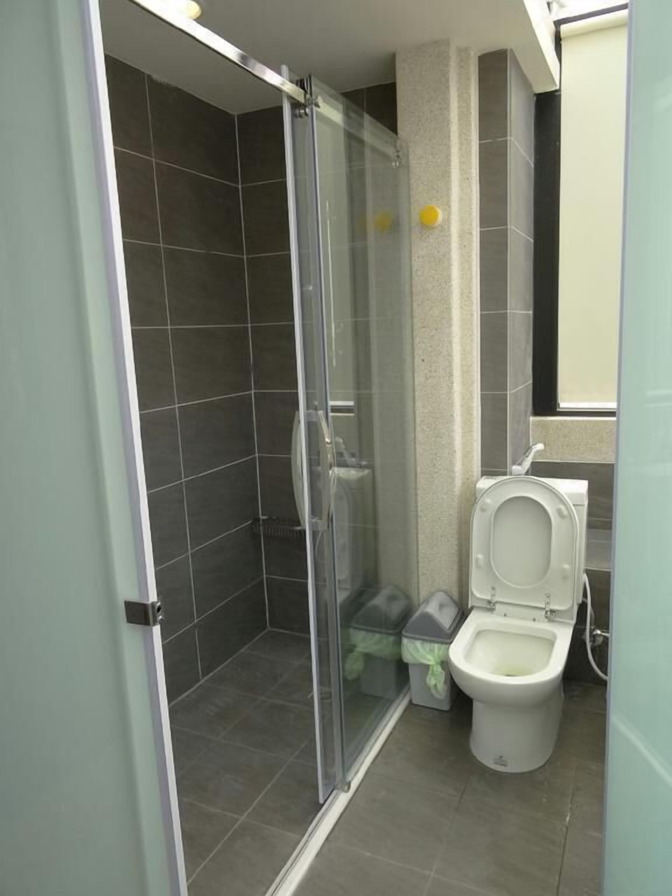 Een badkamer met een douche met glazen wand, een toilet en een prullenbak.