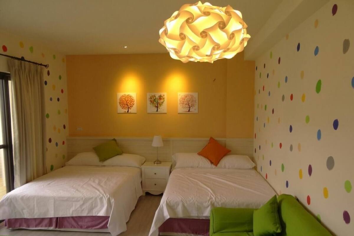 Een hotelkamer met twee bedden, een groene bank, een decoratieve plafondlamp en wanddecoratie.
