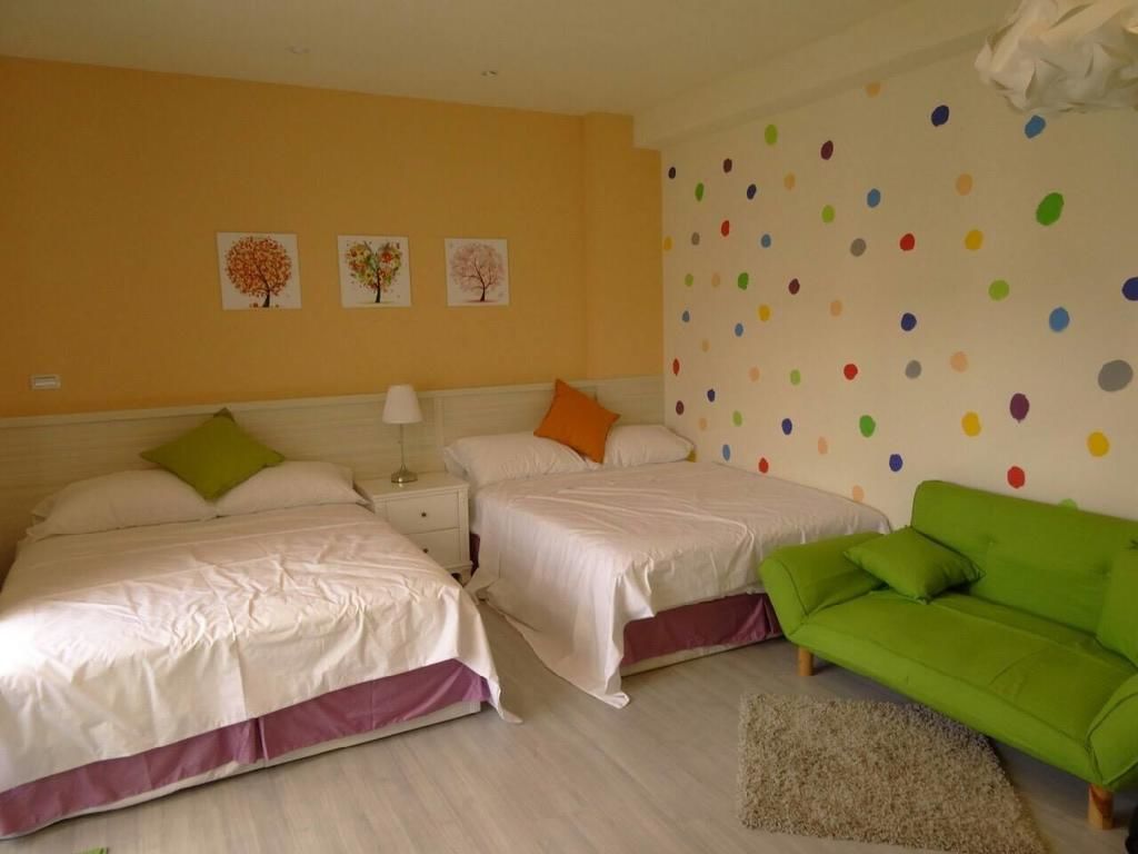 Habitación de hotel con dos camas, un sofá verde y una pared con lunares de colores.