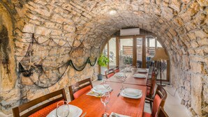 An arched stone ceiling with a dining table set for six, surrounded by wooden chairs with red cushions.