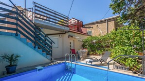 A swimming pool with a blue deck, a staircase with blue railings, and a red chair.