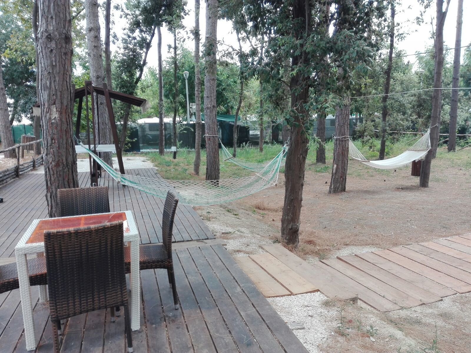 Una terraza de madera con muebles de mimbre y hamacas, rodeada de árboles.