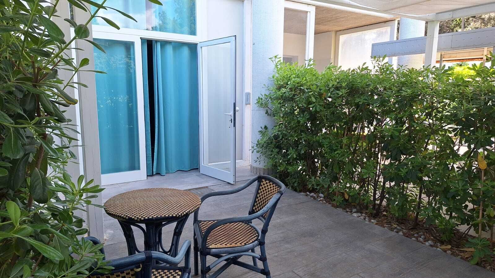 A patio with a table and chairs, a sliding glass door, and a hedge.