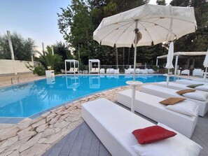 A swimming pool with white lounge chairs and umbrellas, surrounded by stone tiles and greenery. - Biancopineta B&B (San Salvo)